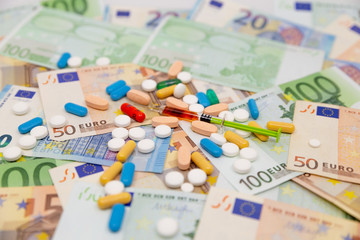 Spread Stack of Euro Banknotes with syringes and pills on top of them, health costs concept