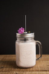Healthy strawberry smoothie or drink yogurt in a mason a jar glass with berries and mint, over a rustic wood table and black background