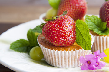 Fresh strawberry fruits over homemade muffins on white  plate decorated with mint leaves. Homemade dessert isolated. 