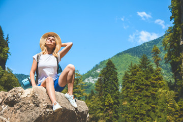 Beautiful Girl Traveler sits on a mountain and enjoys the sun on a background of mountains