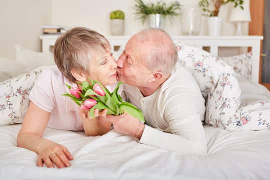 Senior küsst Frau und schenkt Blumen