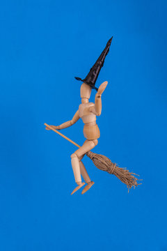 Halloween waving witch riding a broom wearing a black witches hat on solid blue backdrop