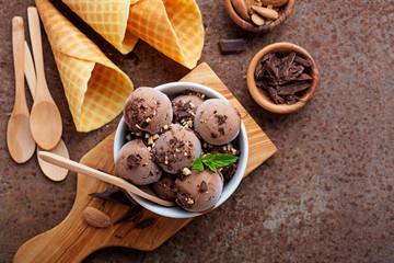  Chocolate ice cream scoops with pieces of chocolate bar and waffle cones on brown background.