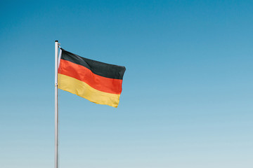 German flag developing in the wind against the blue sky.