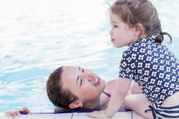 Summer holiday concept. Happy mother and her little daughter playing in swimming pool