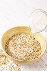 Oatmeal flakes in a wooden bowl on a white background. Milk pours into a bowl of cereal. Vertically.