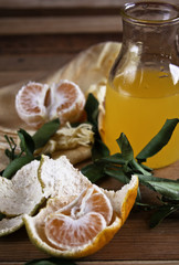 Glass jar with tangerine juice on the rustic wooden table and some tangerines open on the table