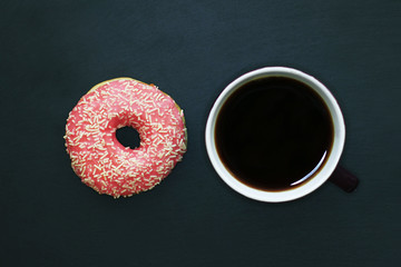Donut in pink glaze and  cup of coffee on  dark background, view from above