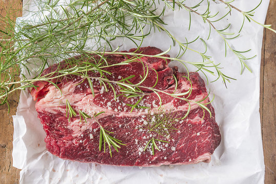 Beautiful raw beefsteak with sea salt, rosemary and dill on white paper top view