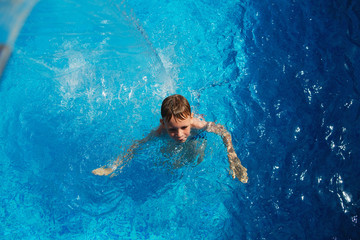 Happy kid playing in blue water of swimming pool on a tropical resort at the sea. Summer vacations concept. Cute boy swimming in pool water