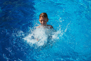 Happy kid playing in blue water of swimming pool on a tropical resort at the sea. Summer vacations concept. Cute boy swimming in pool water