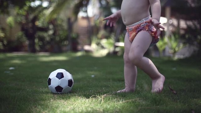 A two-year-old boy likes to play football in the park, run and kick the ball.