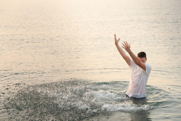A young man standing on the waist in the sea created a very high wall of splashes with the movement of his hands