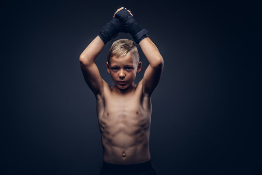 Young shirtless boy boxer wearing sports gloves posing in a studio.