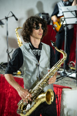 Obraz na płótnie Canvas young artist playing the saxophone. Musical show with musical instrument, young boy with sunglasses and curly hair playing his instrument