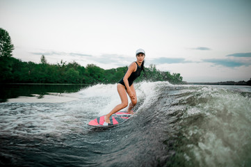 Young attractive woman riding on the orange wakesurf on the river