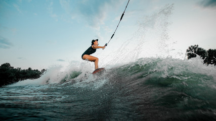 Young attractive woman riding on the wakesurf holding a rope of a motorboat