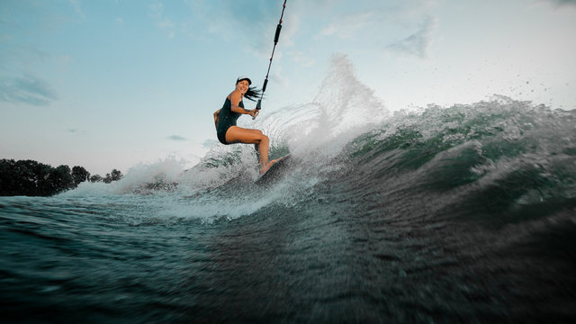 Young beautiful woman riding on the wakesurf holding a rope of a motorboat - Powered by Adobe