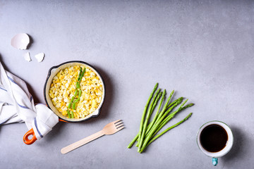 Scrambled eggs with asparagus and coffee in vintage frying pan on the table