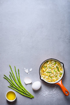 Healthy breakfast. Pan of fried scrumbled eggs with asparagus on grey background