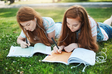 Making homework can be fun. Outdoor shot of two attractive redhead girls with freckles, lying on...