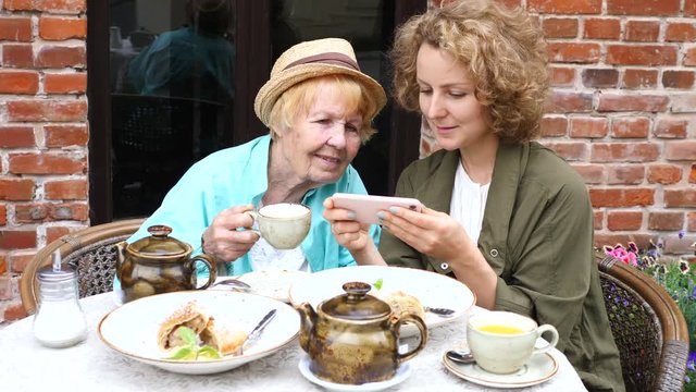 Granddaughter Teaching Grandma How To Use Smartphone In Cafe