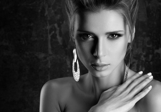 Black and white closeup portrait of young beautiful woman with sensual look. Professional makeup and large earrings. The hand on the shoulder