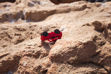 Obraz premium Tiny red car lying upside down on rocky mountain.