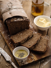 Sliced homemade rye bread on a wooden background with butter and honey.