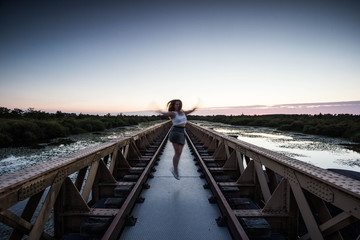 Fashion brunette woman jumping on a urban bridge with sunset happy healthy life