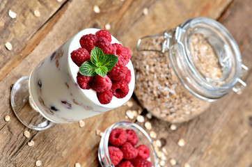 Homemade yoghurt with oatmeal and fresh raspberries in a glass and mint leaves, full glass of oatmeals in background