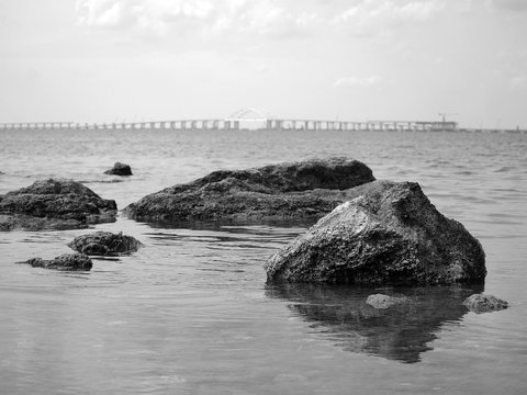 Fototapeta Sea, rocks, bridge in the background. Black and white photography emphasizes the contrast between stone and water.