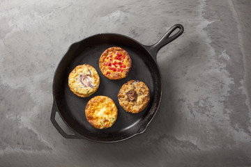 A cast iron pan containing  four freshly cooked quiches on a dark slate effect surface