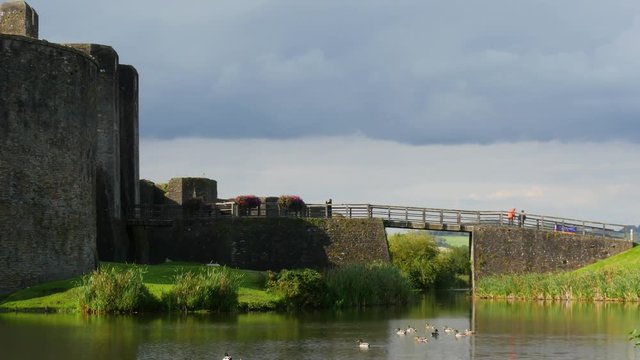 Tourists enjoy visiting Caerphilly Castle and the historic site while ducks swim in the moat.