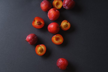 Red sweet cherry plums on dark background, whole and halved. Overhead view