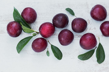 Fresh plums with leaves on white rustic wooden table background.