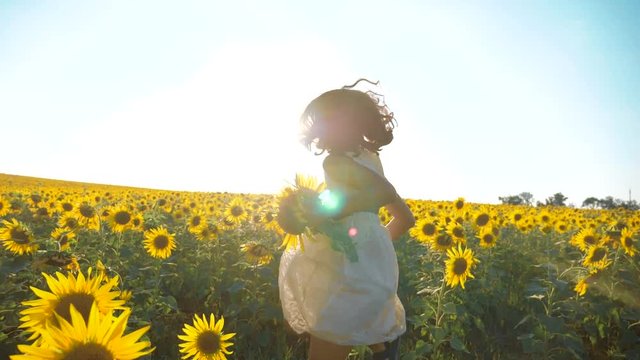 Happy little girl running happy free across the field with sunflowers. slow motion video . smelling big sunflower on summer field. Delight of a pleasant smell. Summer holiday. concept happiness girl