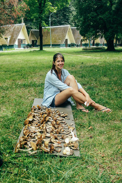 happy stylish girl traveler sitting at pile of gathered mushrooms and smiling, leisure in summer mountains