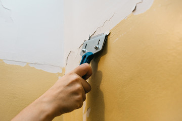 Close-up. A man with a scraper removes the old covering from the wall for further repairs. Wall...