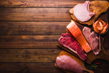 Group of animal proteins, chicken, meat, fish and pork on a wood background