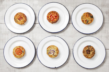 Individual quiches on white enamel plates on a light coloured tabletop