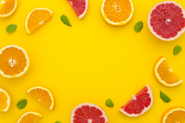 Fototapeta na wymiar A frame made of juicy and fresh citrus fruits with little mint leafs on bright yellow vibrant flat lay background for summer offers. Use it for your hand lettering mockup