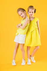 The girls of the twins stand together on a yellow background.