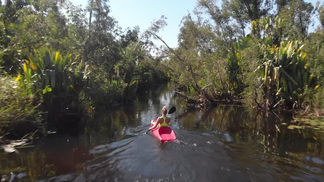 Blonde girl paddling in a red kayak through a rainforest
