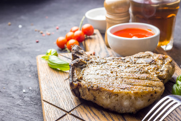 Grilled Steak on bone with knife and fork carving set on black concrete background. Selecrive focus