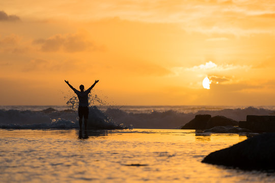 Silhouette of Man with Arms in Air Being Splashed by Surf at Sunset