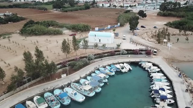 Aerial drone shot of a church in Ayla Napa Cyprus and zoom out to reveal boats docked in the bay