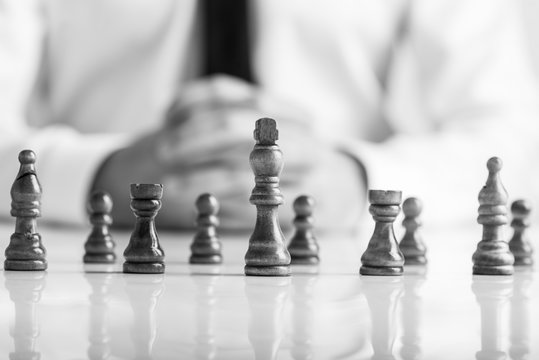 Monochrome image of businessman sitting in front of dark chess pieces