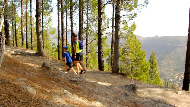 Two men and kid hiking on forest on sunny day in Gran Canaria, Spain. Group of hikers on their way up to Roque Nublo famous monolith landmark in Canary Islands. Adventure, outdoor activity concepts