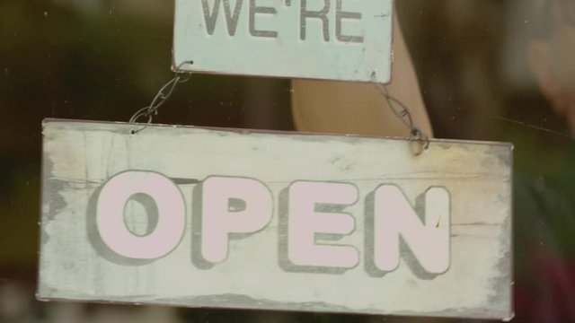 Man turning close sign to open in the storefront window